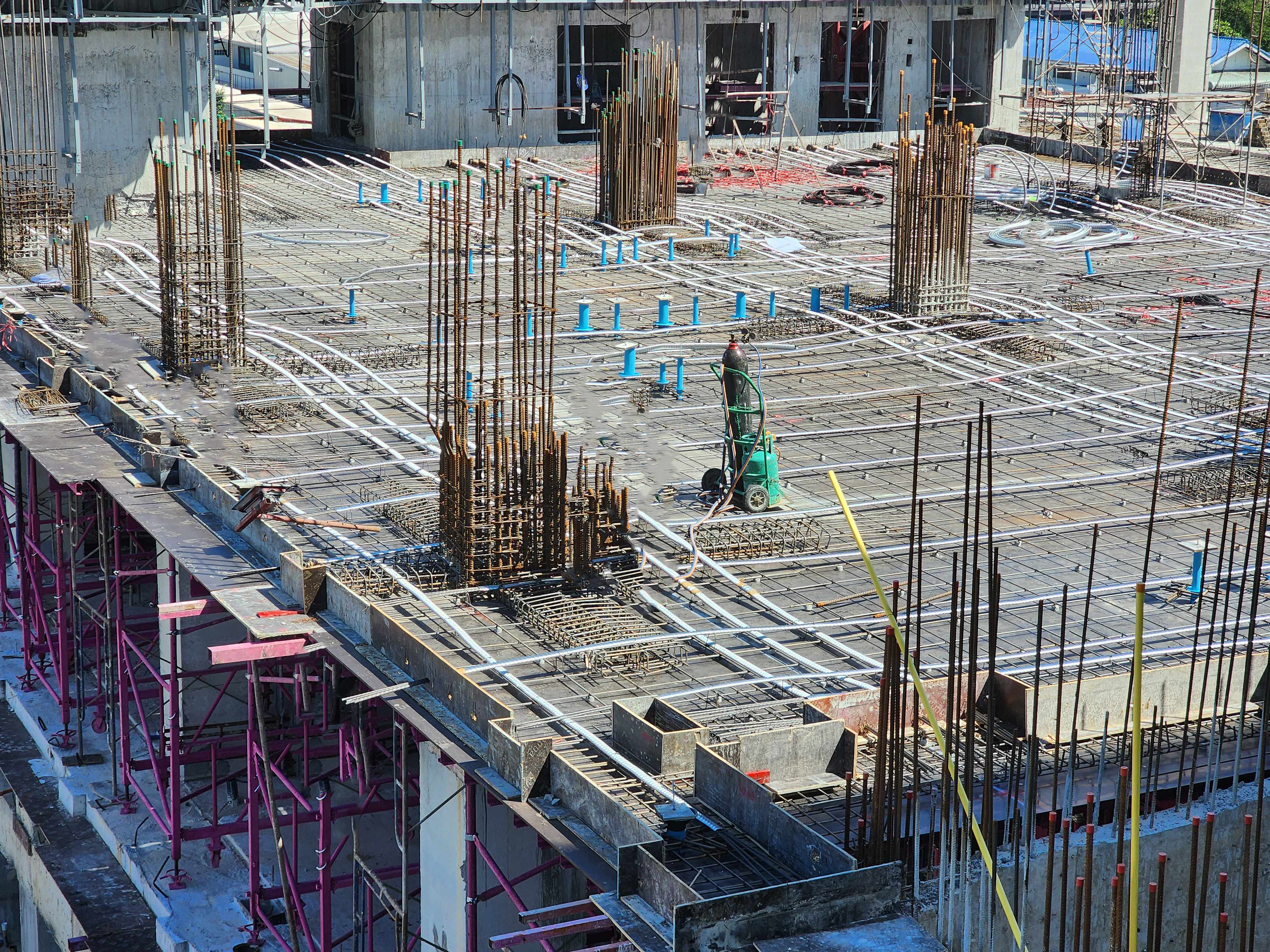 Construction site showing concrete slab with blue spray paint markings indicating embedded rebar and utilities located through concrete scanning